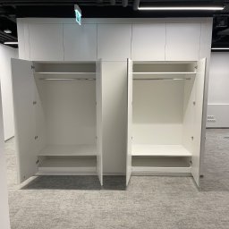 ARTmeble - Biała szafa wnękowa z otwartymi drzwiami, widoczne półki i drążek na ubrania. Na podłodze leżą narzędzia. Sufit z instalacjami.