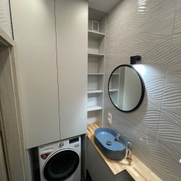 ARTmeble - Kompaktowa łazienka z pralką LG w zabudowie, jasnoszarymi szafkami, drewnianym blatem i owalną, niebieską umywalką. Ściana z lustrem pokryta falistymi płytkami.