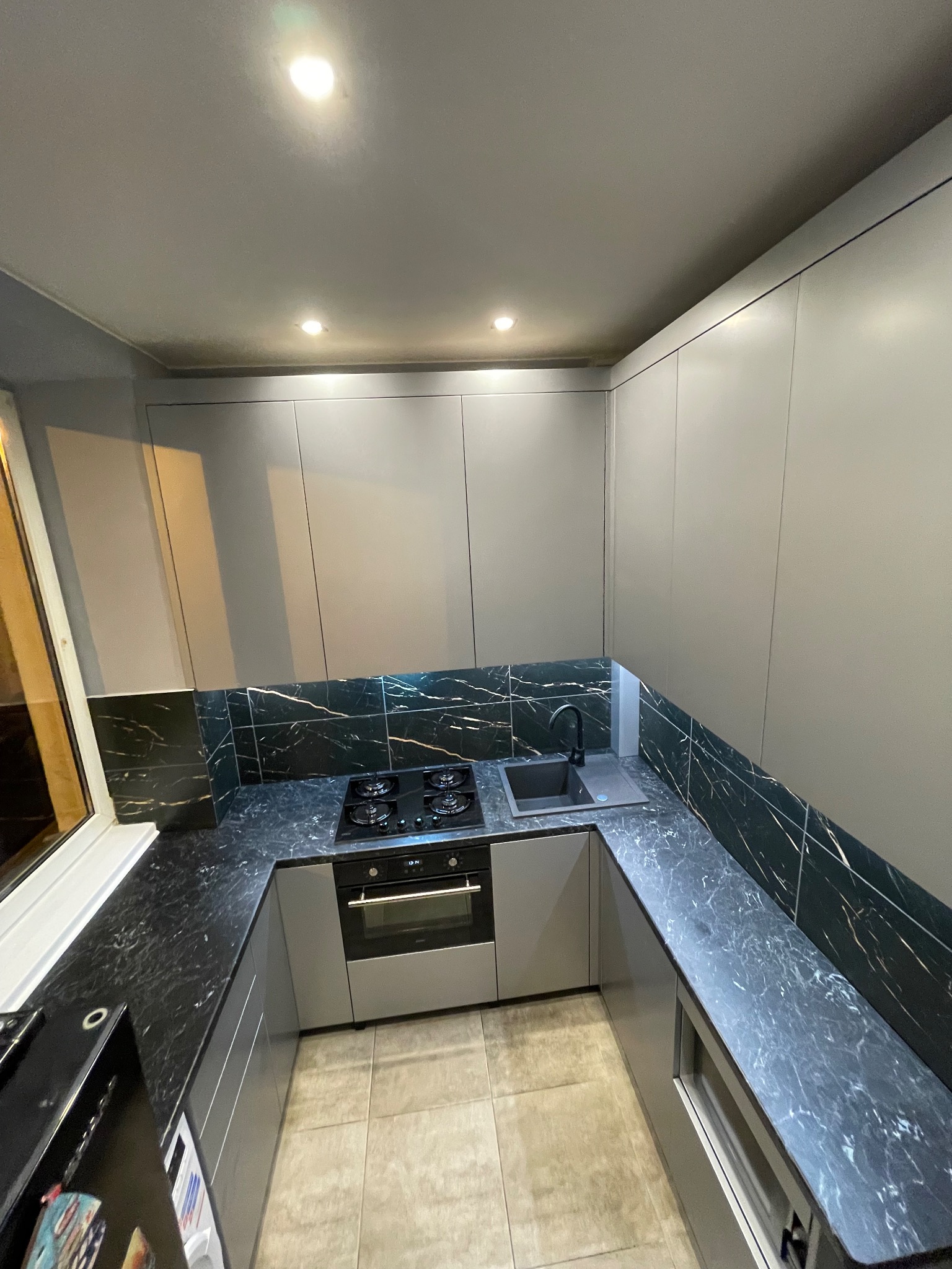 Nowoczesna kuchnia w szarościach z czarnym blatem i backsplashiem imitującym marmur. Ujęcie z góry podkreśla układ zabudowy i oświetlenie punktowe.