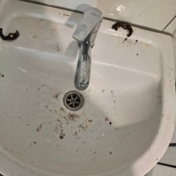 Domowa Harmonia - Zabrudzona, biała umywalka z chromowaną baterią Ferro przed czyszczeniem. Widoczne zaschnięte plamy i resztki zabrudzeń. Ujęcie z góry.