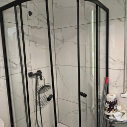 Domowa Harmonia - Narożna kabina prysznicowa z czarnymi profilami na tle marmurowych płytek. Widoczne akcesoria i niedoskonałości przed sprzątaniem.