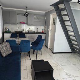 Domowa Harmonia - Wnętrze po sprzątaniu: szaro-biała kuchnia z niebieskimi krzesłami i kanapą, marmurowe płytki podłogowe, minimalistyczne schody. Widok na czysty, uporządkowany pokój.