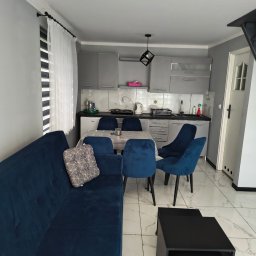 Domowa Harmonia - Nowoczesne wnętrze po sprzątaniu: szare szafki kuchenne, niebieskie krzesła i sofa, stół w kratę, marmurowe płytki podłogowe. Widok ogólny.