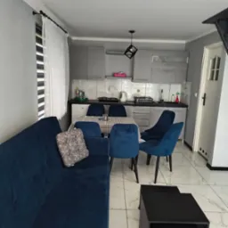 Nowoczesne wnętrze po sprzątaniu: szare szafki kuchenne, niebieskie krzesła i sofa, st&oacute;ł w kratę, marmurowe płytki podłogowe. Widok og&oacute;lny.