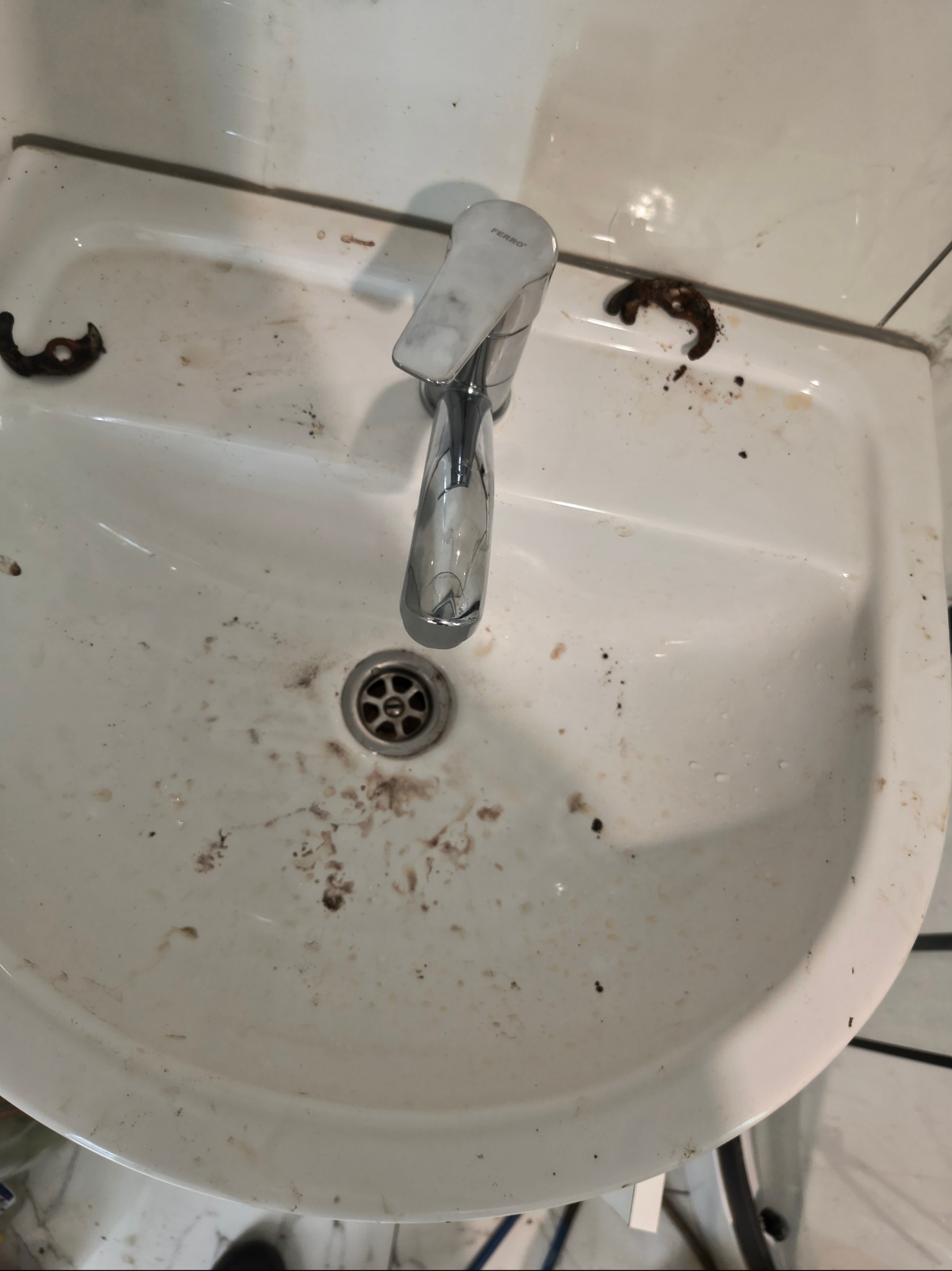 Zabrudzona, biała umywalka z chromowaną baterią Ferro przed czyszczeniem. Widoczne zaschnięte plamy i resztki zabrudzeń. Ujęcie z góry.