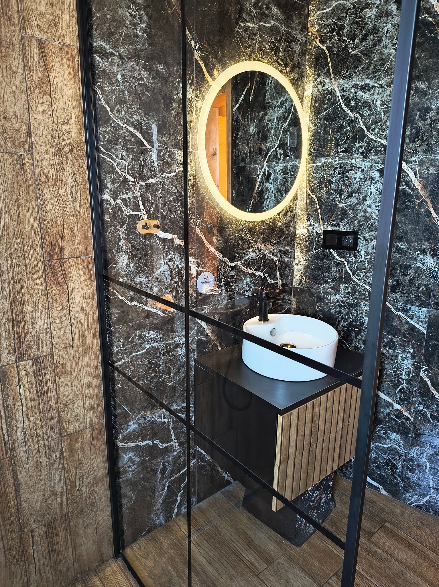 Nowoczesna łazienka po remoncie: marmurowe płytki, okrągłe lustro z podświetleniem LED i minimalistyczna umywalka nablatowa z czarną armaturą.