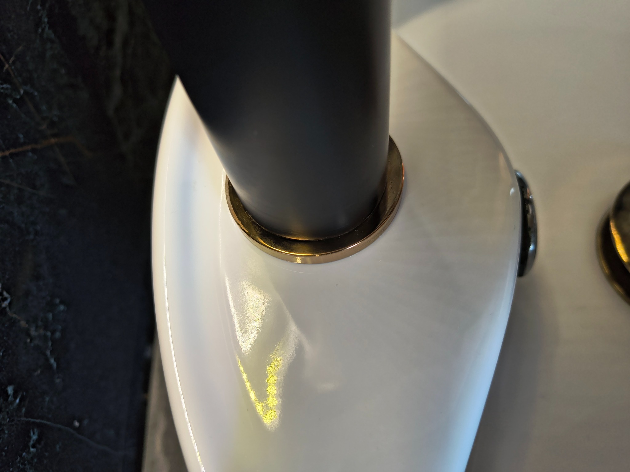 Błyszcząca, biała umywalka z czarną armaturą i złotymi detalami, po sprzątaniu. Widoczny fragment marmurowej ściany.