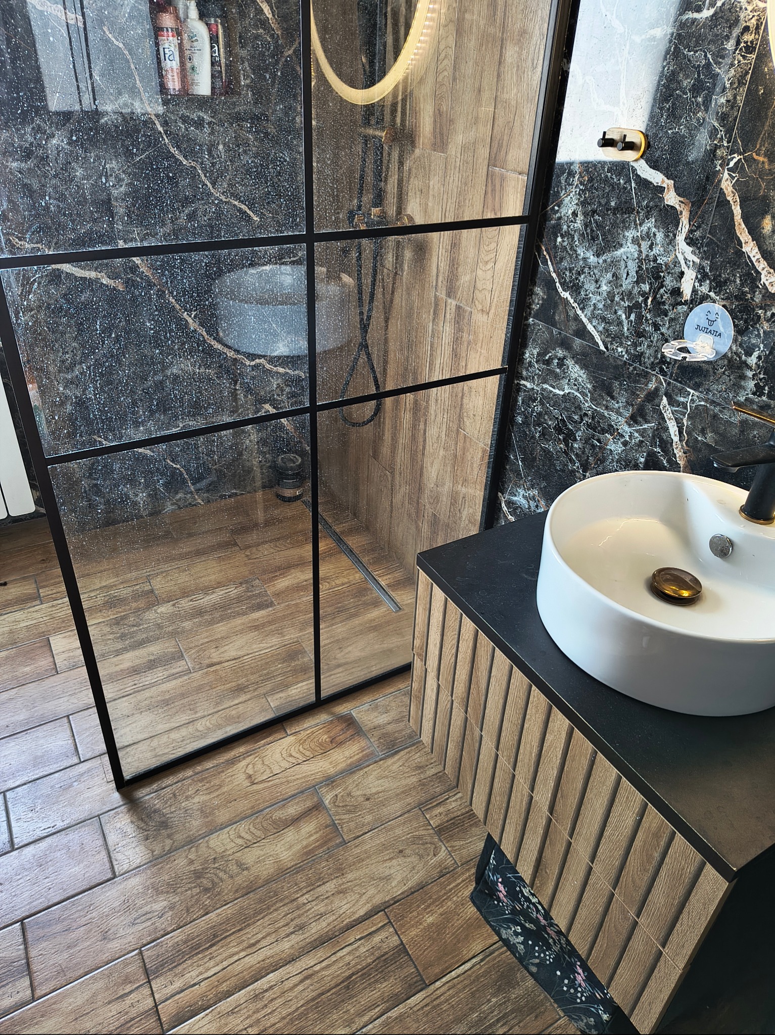 Wnętrze łazienki z kabiną prysznicową typu walk-in, umywalką nablatową i marmurowymi płytkami. Widoczne detale wykończenia i armatura.