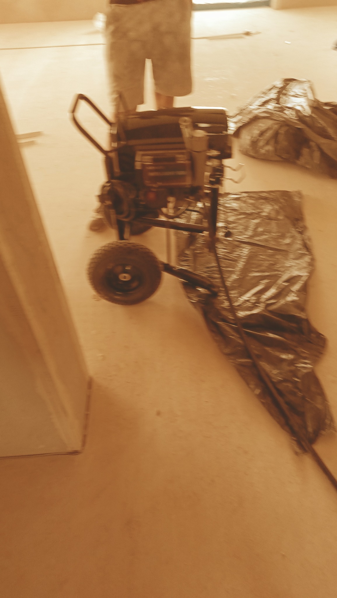 Agregat malarski na kółkach i folia ochronna na podłodze w Sarbicku, przygotowanie do malowania ścian w pomieszczeniu.