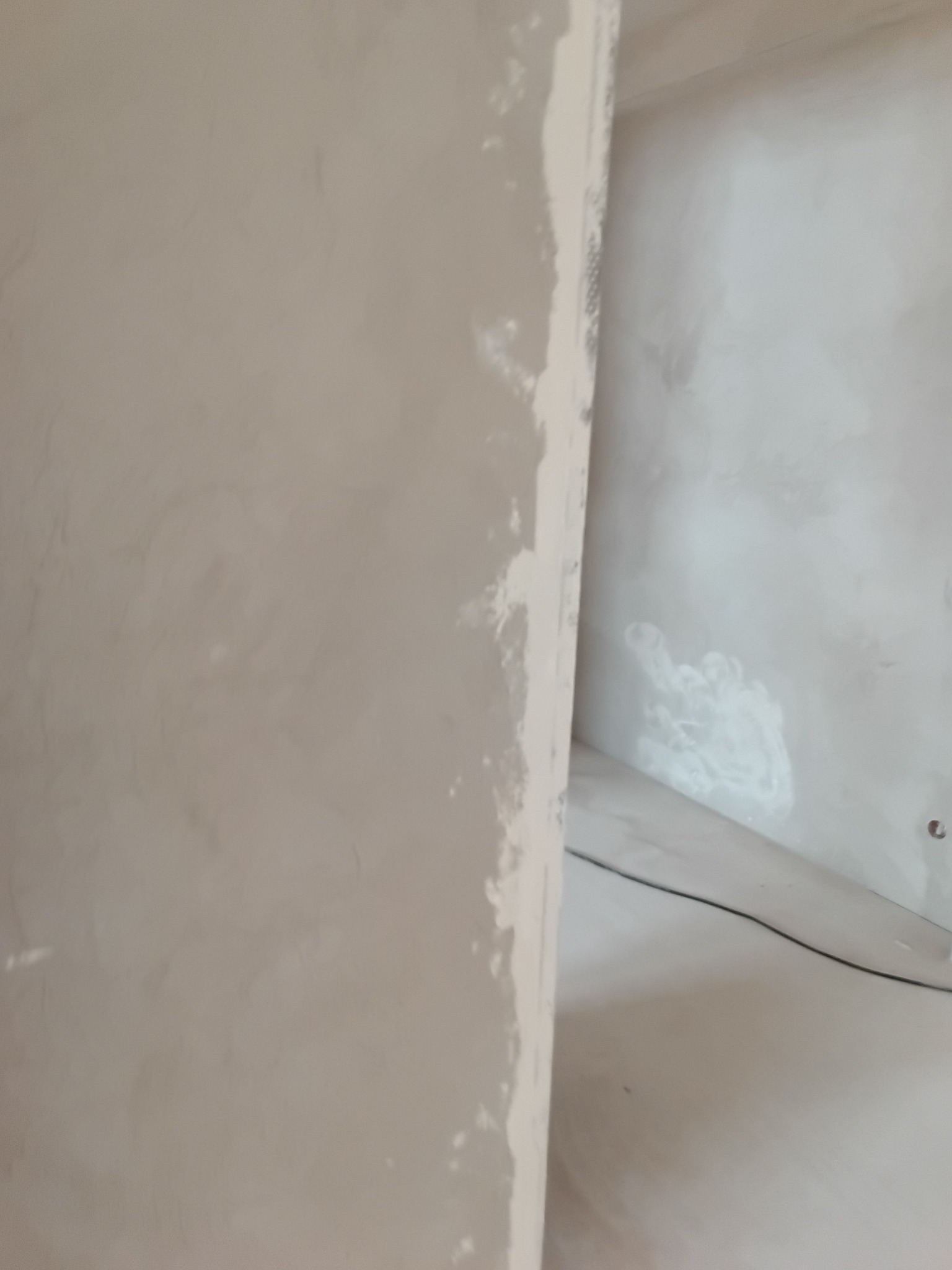 Ściana po szpachlowaniu, widoczne nierówności i ślady po szpachli. Przygotowanie do malowania. Szpachlowana krawędź ściany w zbliżeniu. Jasne wnętrze w trakcie prac wykończeniowych.