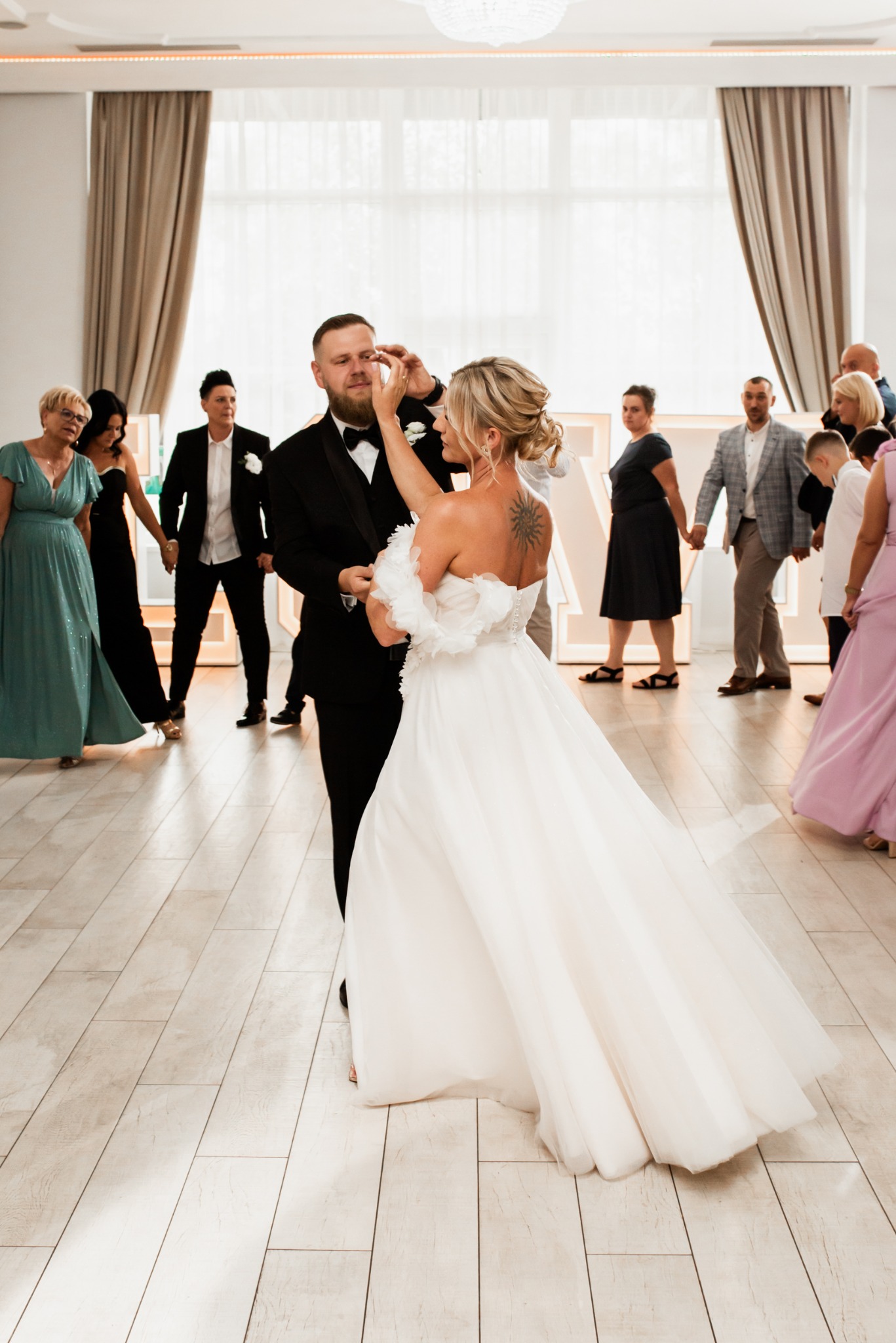 Para młoda w tańcu podczas wesela. Panna młoda ociera łzę panu młodemu. W tle goście i dekoracje sali weselnej.
