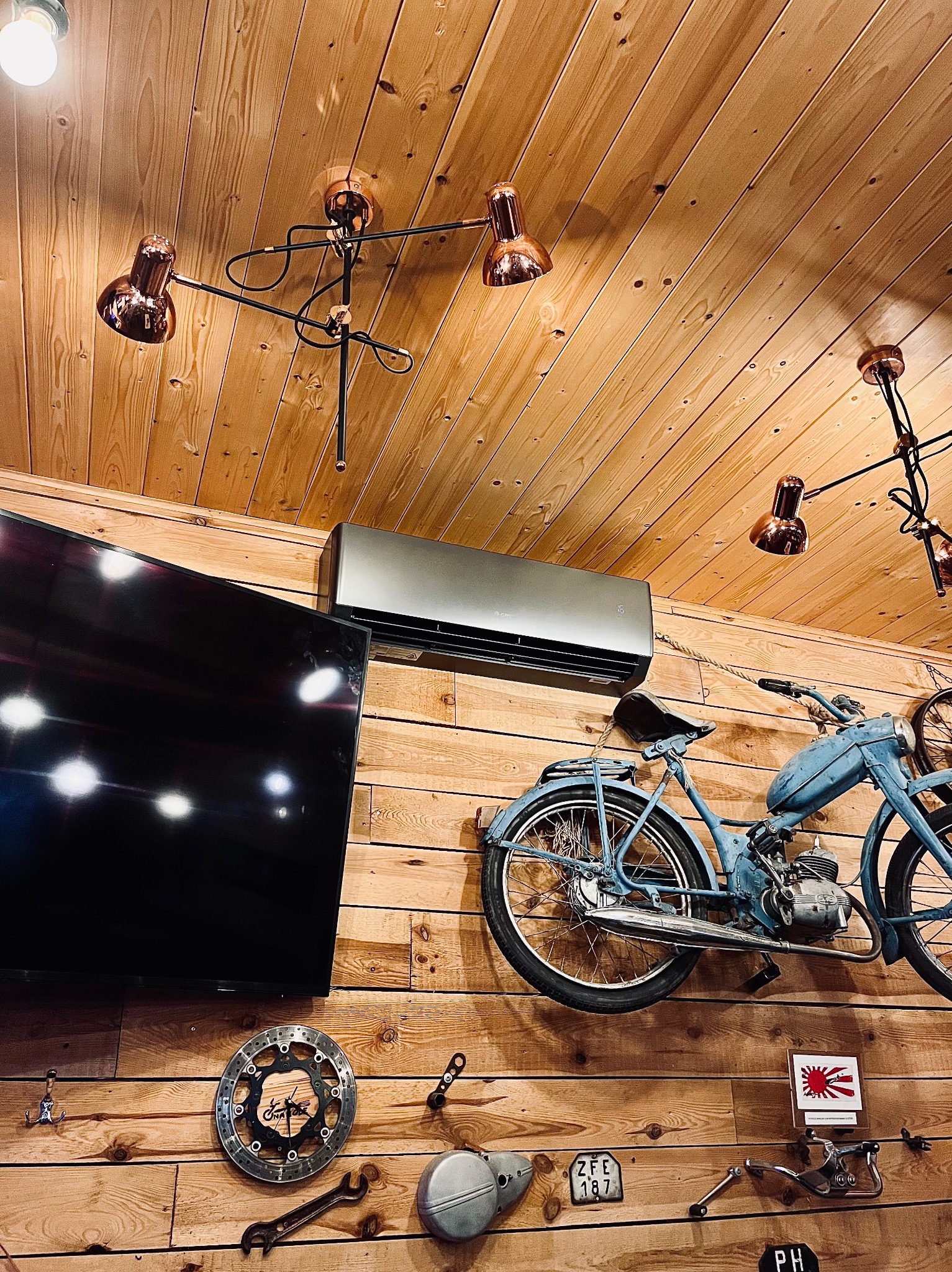 Klimatyzator ścienny w stylowym wnętrzu z drewnianą boazerią, oświetleniem w stylu industrialnym i dekoracyjnym motocyklem. Widok od dołu.