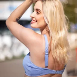 Uśmiechnięta blondynka w błękitnym topie, z tatuażem r&oacute;ży na ramieniu, pozuje w plenerze w Łodzi. Delikatny makijaż i profil twarzy.