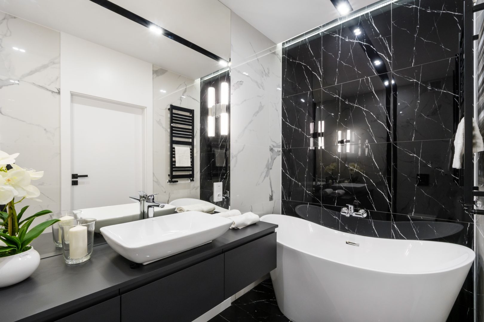 Elegancka łazienka w czarno-białej tonacji: marmurowe płytki, wolnostojąca wanna i nowoczesna umywalka nablatowa. Minimalistyczny design z akcentami kwiatowymi.
