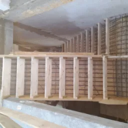 Zbrojenie ściany szalunkiem z desek i siatką z drutu. Widoczne betonowe elementy konstrukcyjne. Etap budowy z bliska, surowy stan.