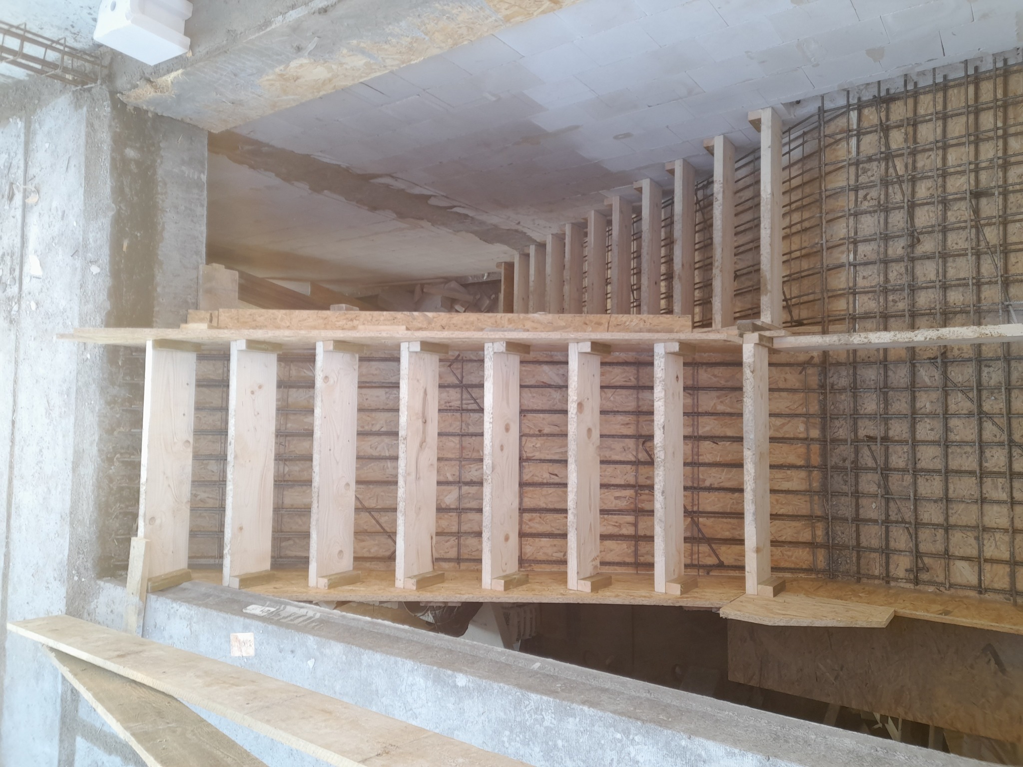 Zbrojenie ściany szalunkiem z desek i siatką z drutu. Widoczne betonowe elementy konstrukcyjne. Etap budowy z bliska, surowy stan.