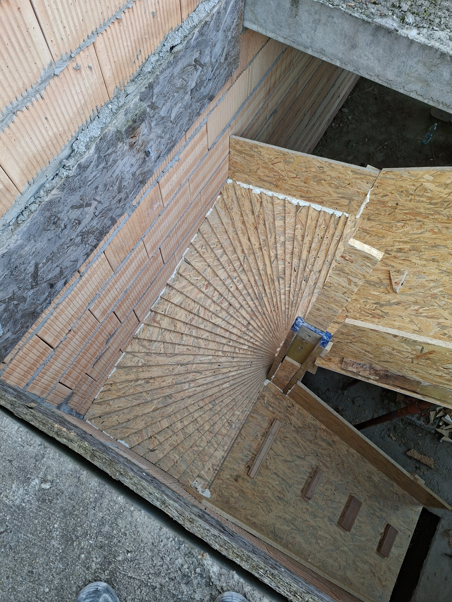 Wykonywanie betonowych schodów spiralnych z deskowaniem w Poznań. Widok z góry na konstrukcję z płyt OSB i murowane elementy. Etap budowy.