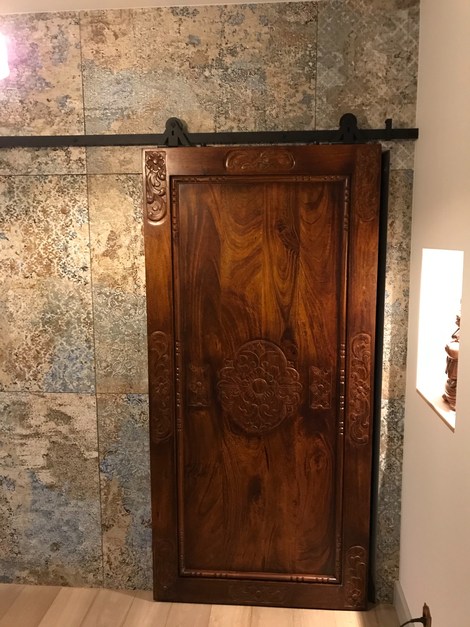 Drewniane, przesuwne drzwi z rzeźbieniami, zamontowane na tle ściany wyłożonej dekoracyjnymi płytkami. Element wykończenia wnętrza.