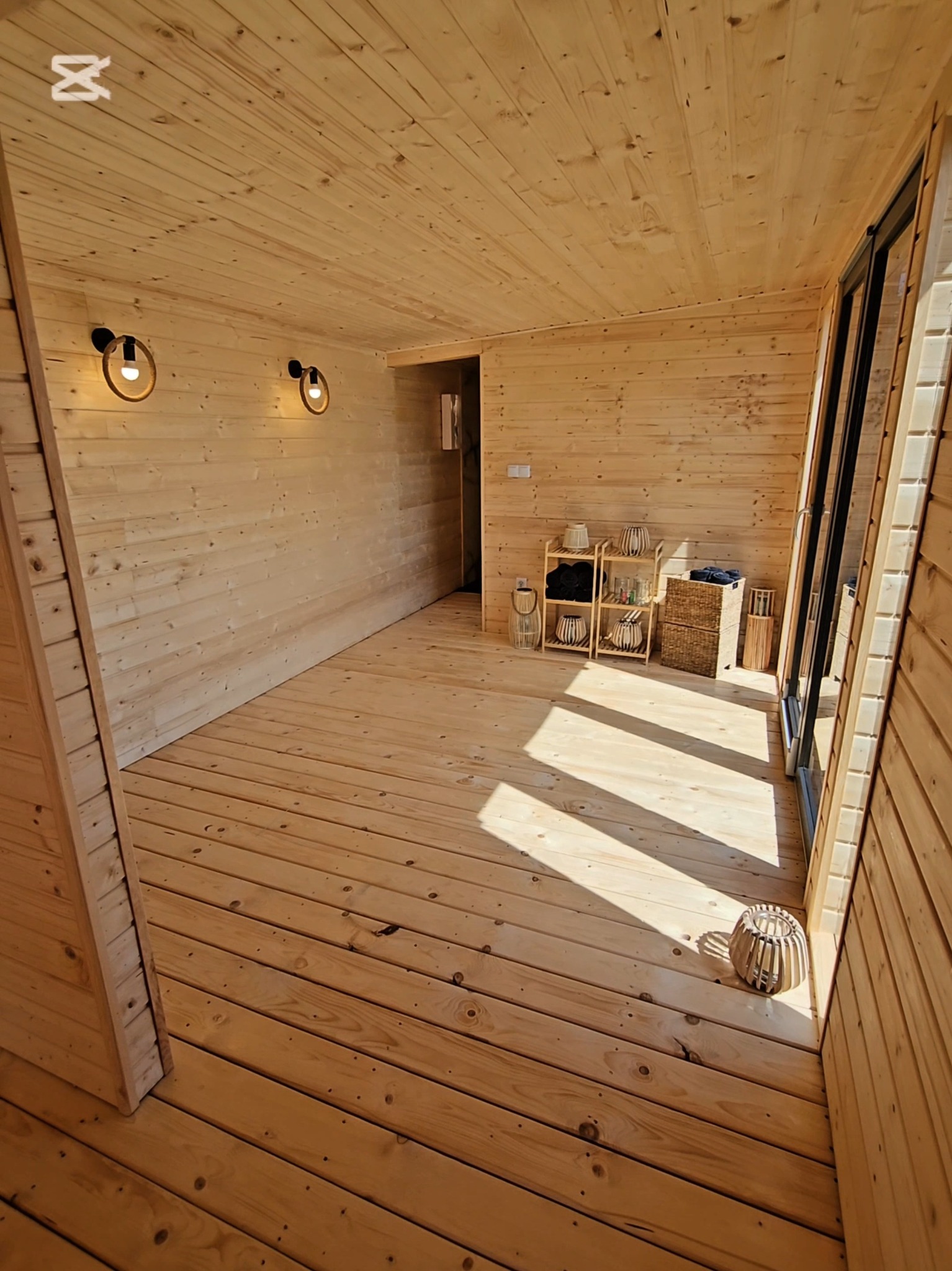 Wnętrze sauny wykończone drewnem, z oświetleniem i półkami na akcesoria. Duże okno wpuszcza naturalne światło, tworząc przytulną atmosferę.