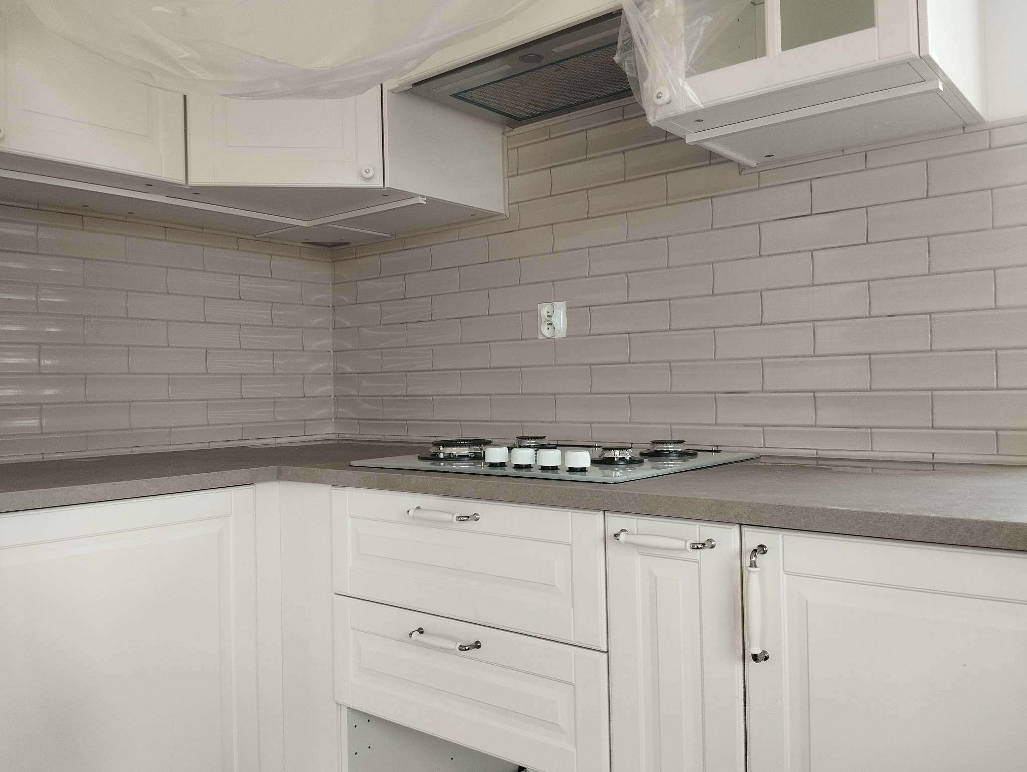 Białe, klasyczne meble kuchenne z szarą, kamienną płytą blatu i płytkami w odcieniach szarości. Na blacie kuchenka gazowa.