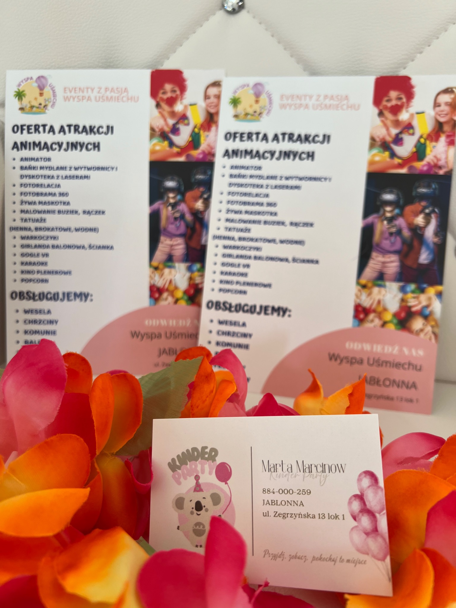 Ulotki z ofertą animacji 'Wyspa Uśmiechu' i wizytówka 'Kinder Party' Marty Marcinów, otoczone dekoracyjnymi kwiatami. Oferta obejmuje m.in. animatora, fotobramę 360, VR.