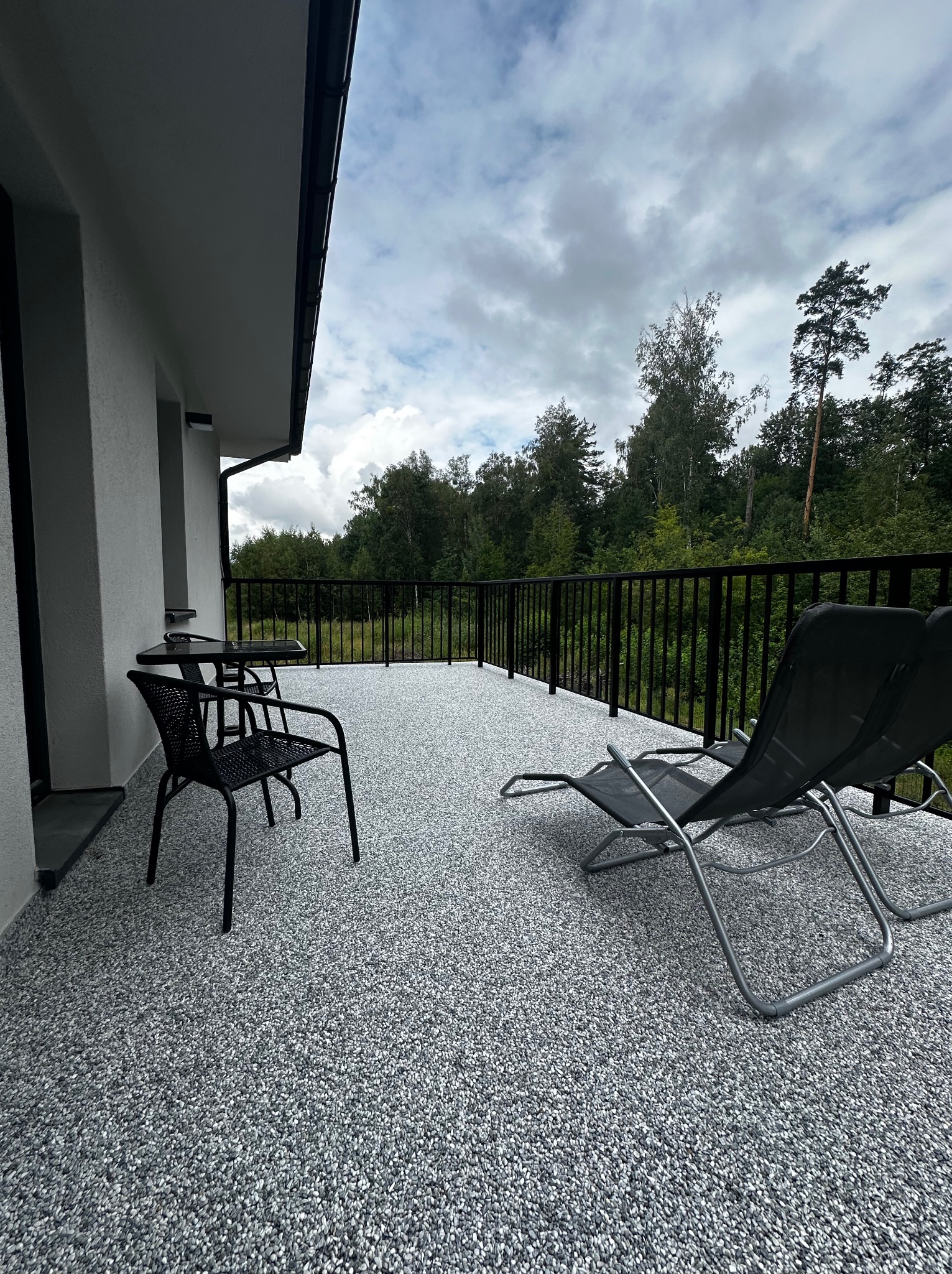 Balkon z szarą posadzką żywiczną, meble ogrodowe i widok na zieleń. Detal wykończenia balkonu z posadzką żywiczną w odcieniach szarości i bieli.