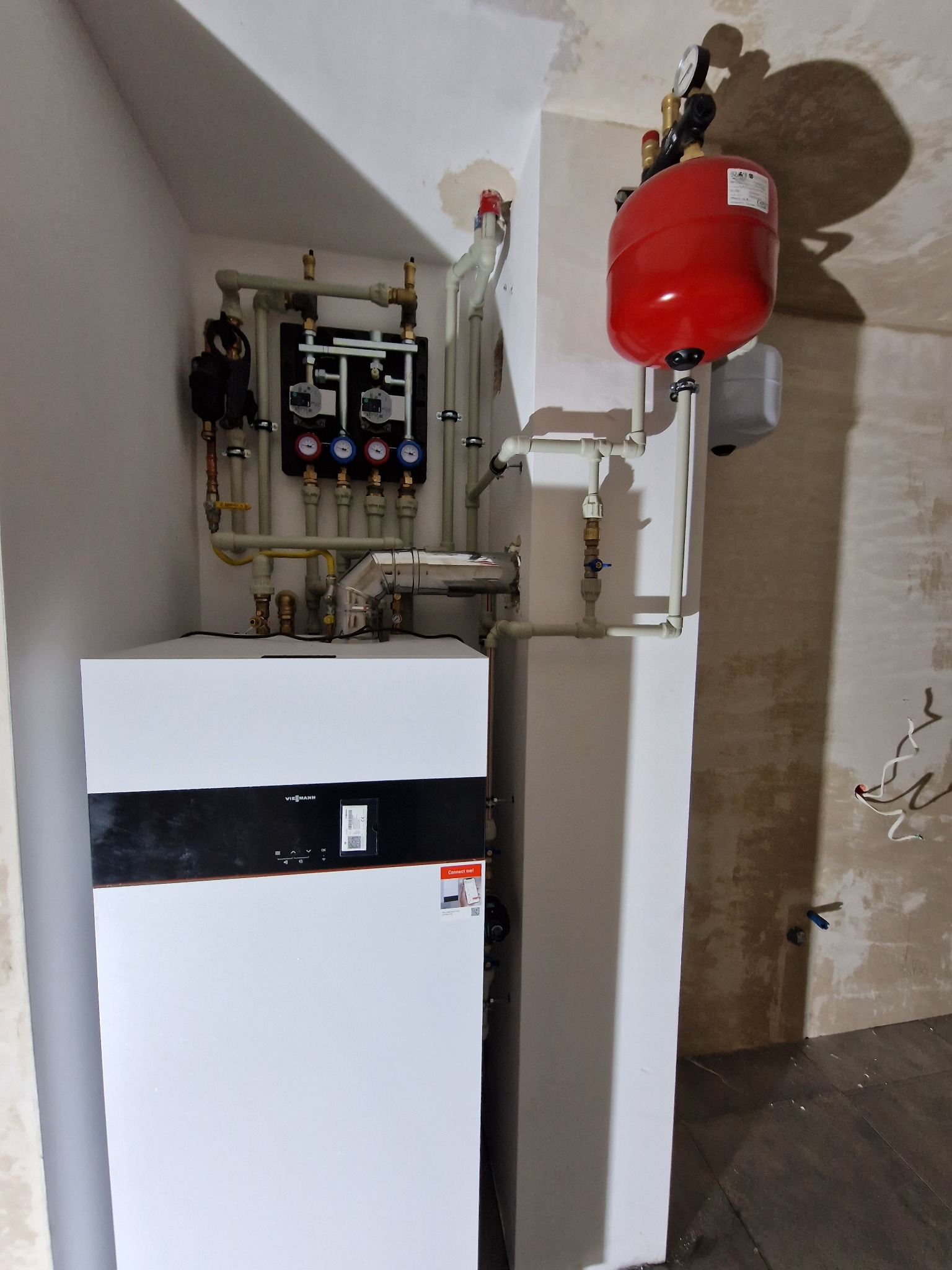 Nowoczesny, biały piec gazowy Viessmann z czarnym panelem, zainstalowany w pomieszczeniu z surowymi ścianami i widoczną instalacją hydrauliczną.