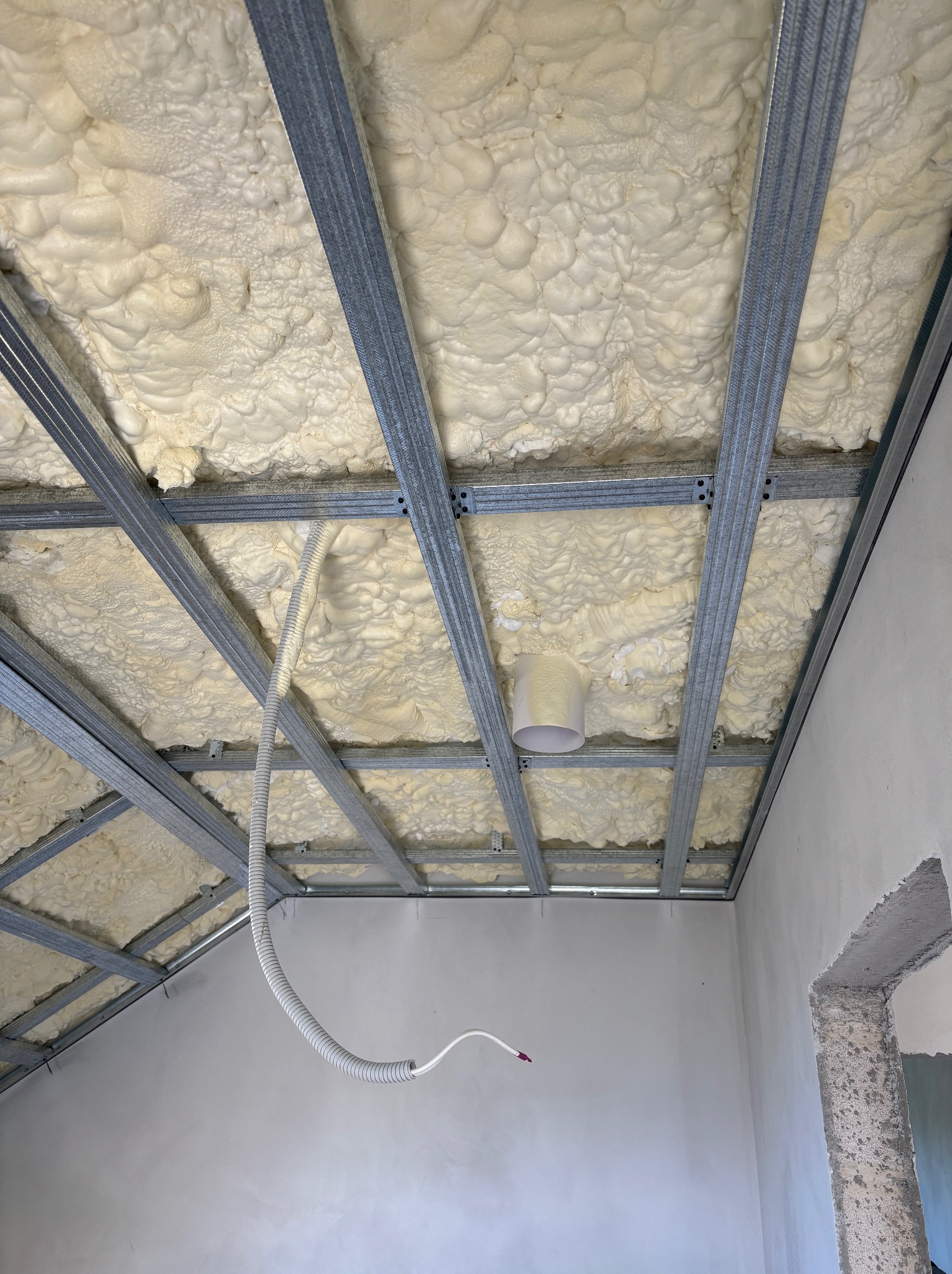 Metalowa konstrukcja sufitu podwieszanego wypełniona pianką izolacyjną, widoczna instalacja elektryczna w peszlu. Surowy stan wykończenia wnętrza.