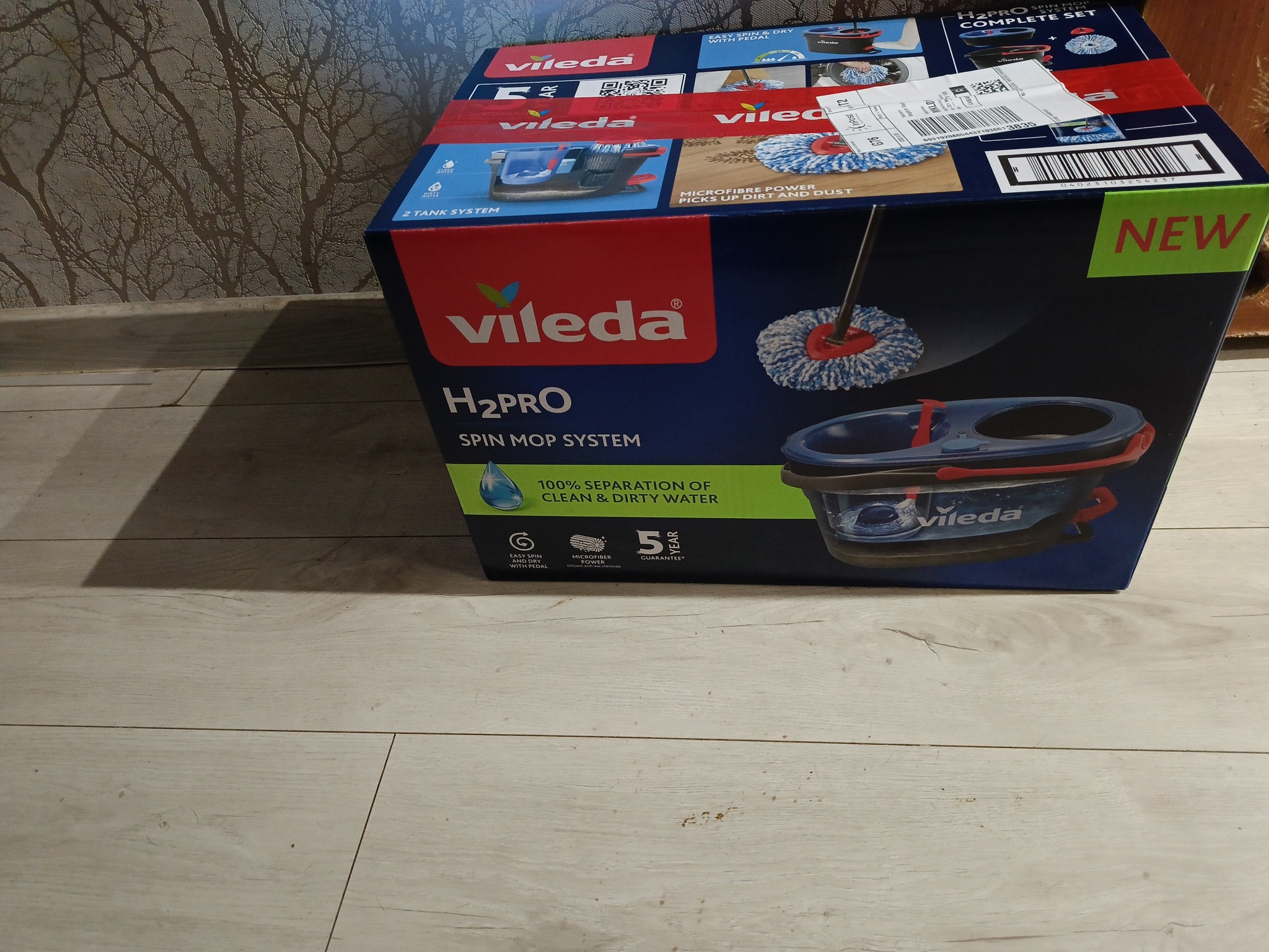 Pudełko z mopem obrotowym Vileda H2Pro Spin Mop System na podłodze. Widoczne logo Vileda, informacje o systemie dwukomorowym i mikrofibrach. Etykieta 'NEW' na rogu.