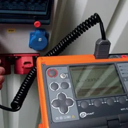 Miernik Sonel MPI-525 w trakcie pomiaru napięcia w gniazdach elektrycznych oznaczonych numerami 1 i 2, ZG2, z widocznym przewodem pomiarowym w dłoni.