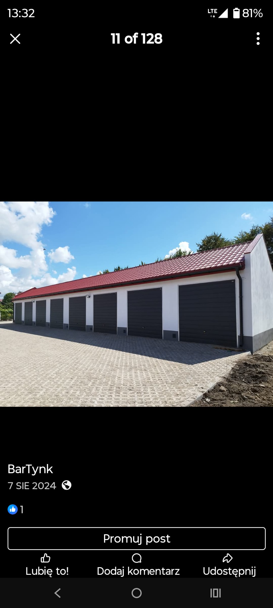 Rząd garaży z czerwonym dachem i szarymi bramami, widok z zewnątrz na kostkę brukową. Budynki otynkowane na biało, w słoneczny dzień.