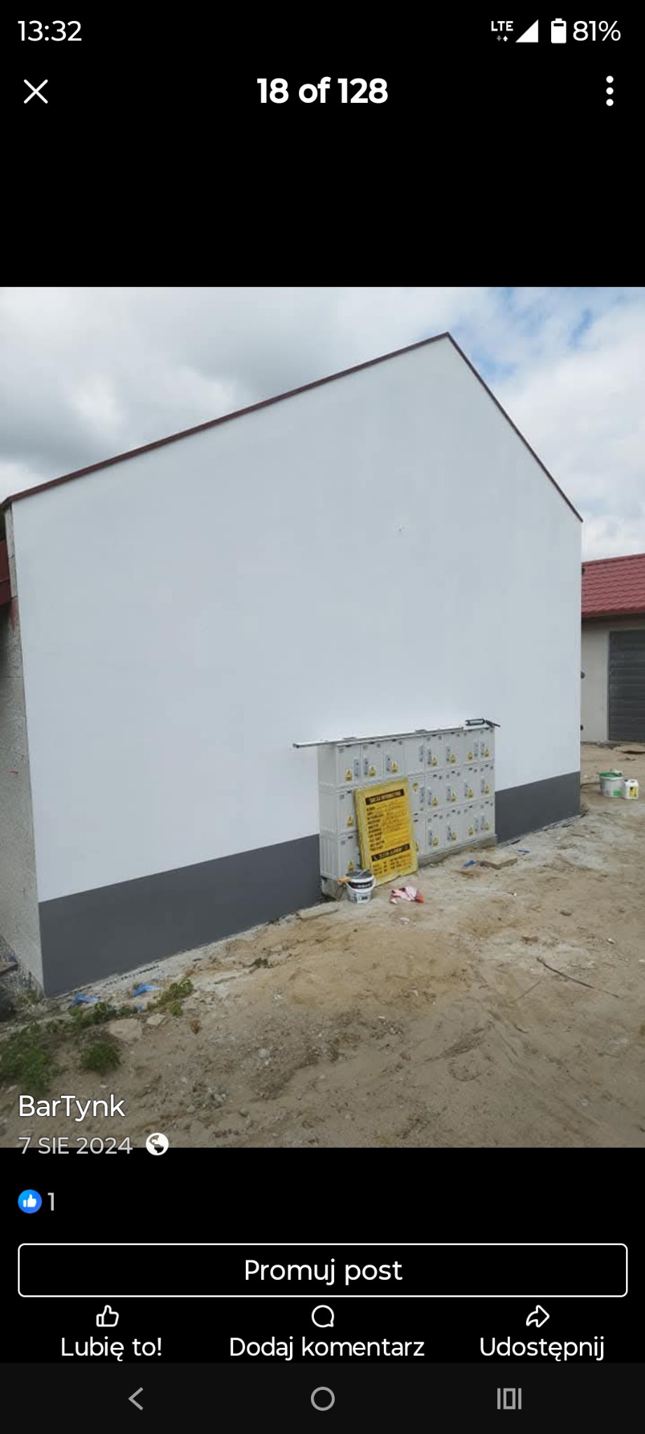 Świeżo pomalowana elewacja budynku z szarą podmurówką. Widoczne puszki z farbą i drabina. Biała ściana kontrastuje z ziemistym otoczeniem.