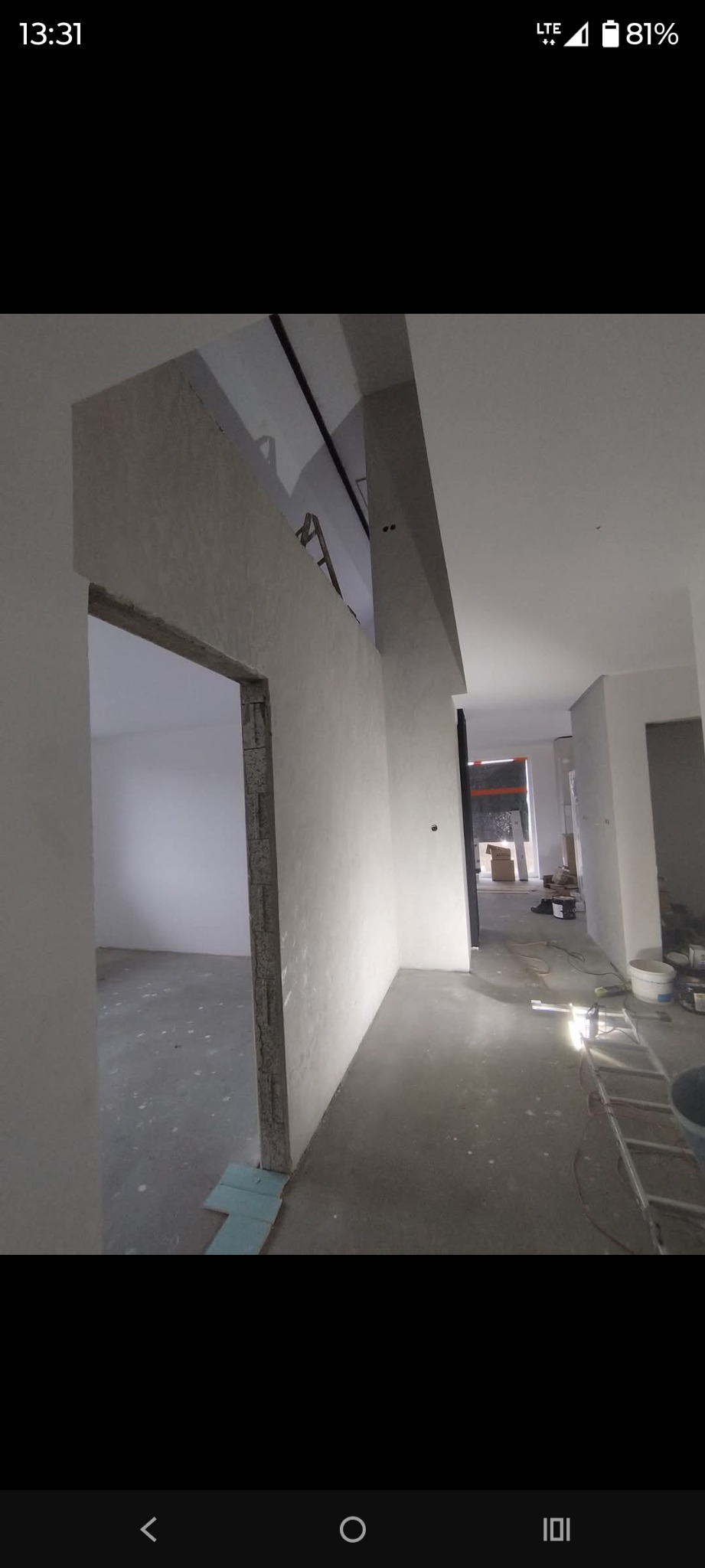 Wnętrze w trakcie prac wykończeniowych: ściany przygotowane pod malowanie, widoczne surowe wnęki drzwiowe, podłoga zabezpieczona. W tle drabina i narzędzia.