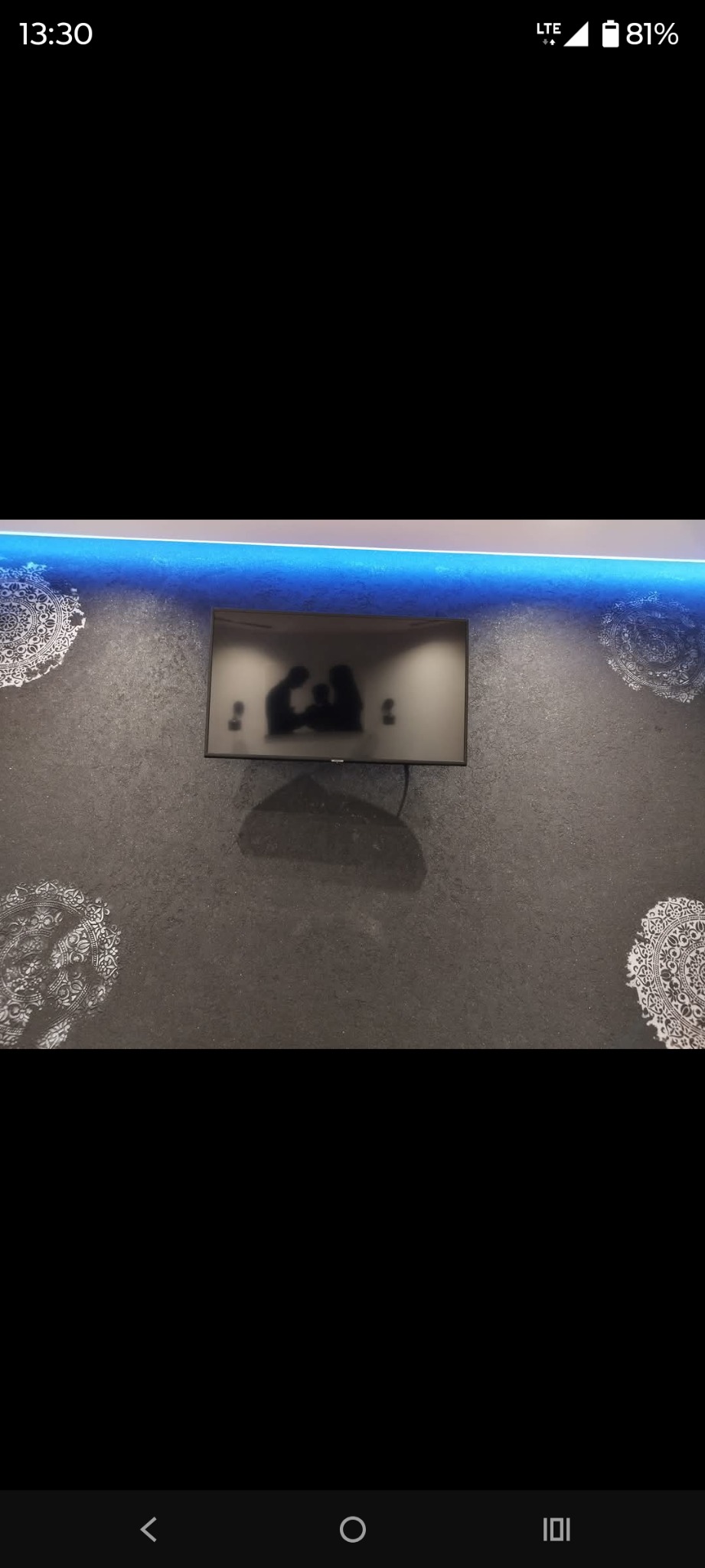 Szara ściana z dekoracyjnymi mandalami i podświetleniem LED w Kętrzynie. Na ścianie wisi telewizor.