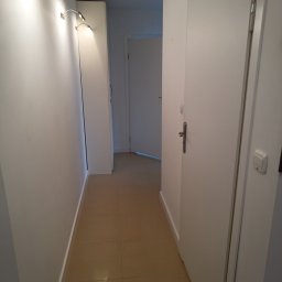 Instal & Serwis Jakub Sikora - Korytarz z beżową podłogą z płytek, białe ściany z oświetleniem punktowym i białe drzwi. Widok na kolejne pomieszczenie.