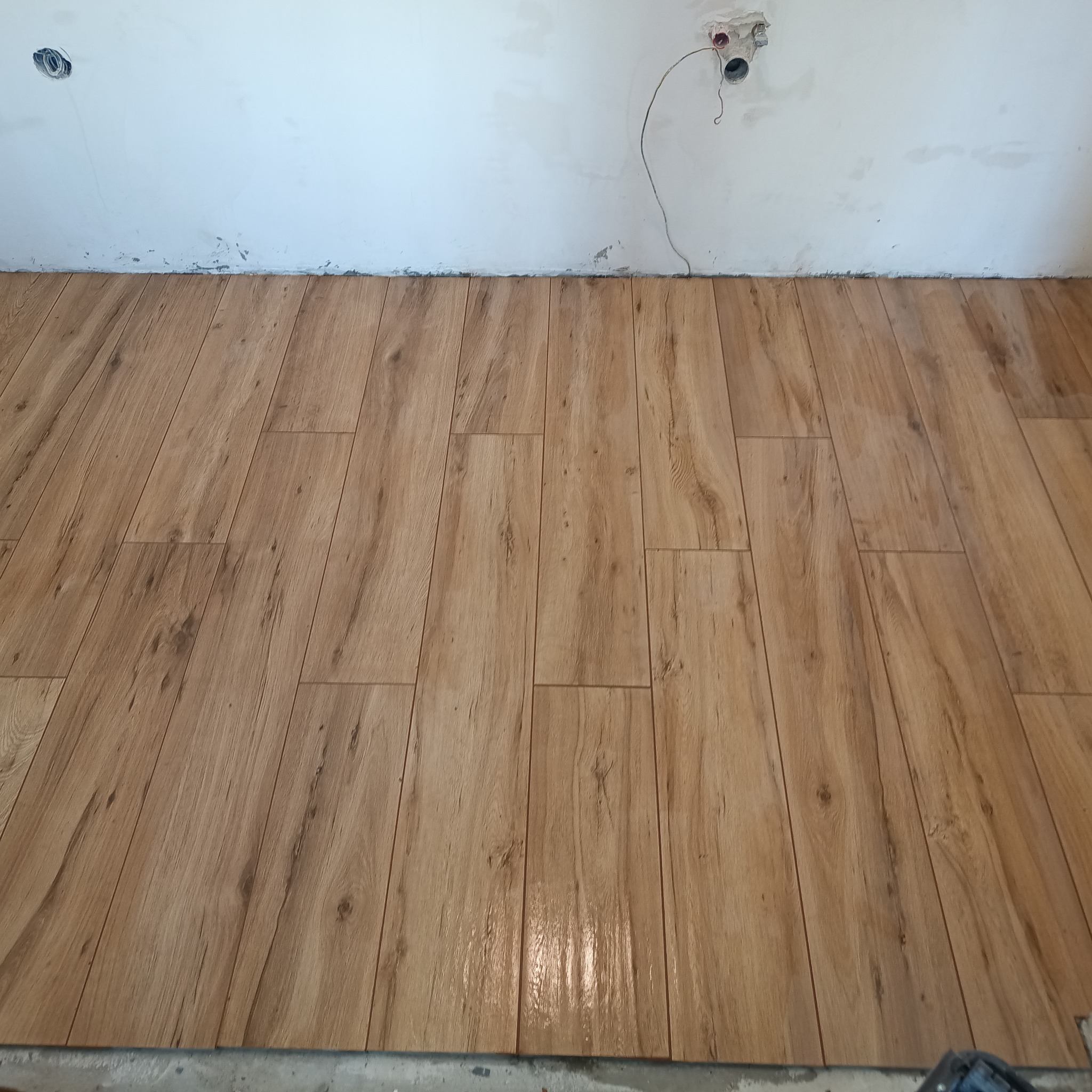 Ułożona podłoga z płytek imitujących drewno, ułożonych pod kątem. Widoczne niedokończone ściany z wystającymi kablami.