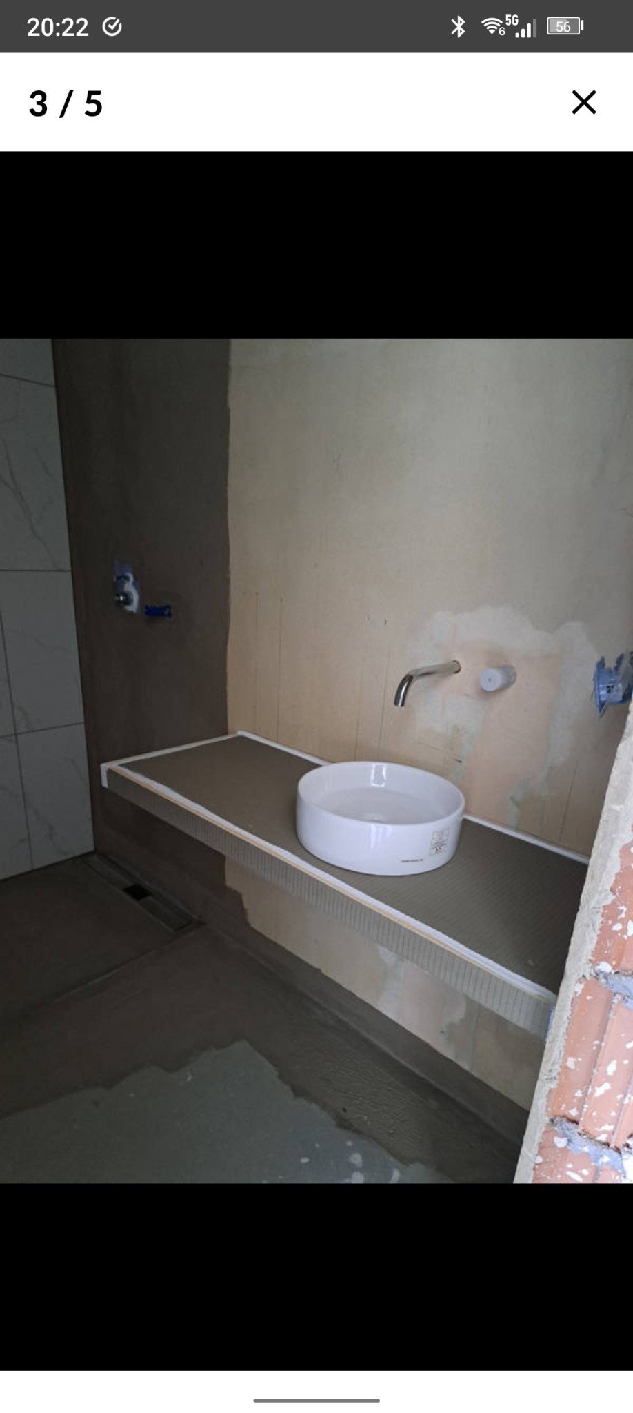 Niedokończona łazienka z umywalką nablatową na blacie z płytek. Widoczne surowe ściany, fragmenty płytek i instalacji. Etap prac wykończeniowych.