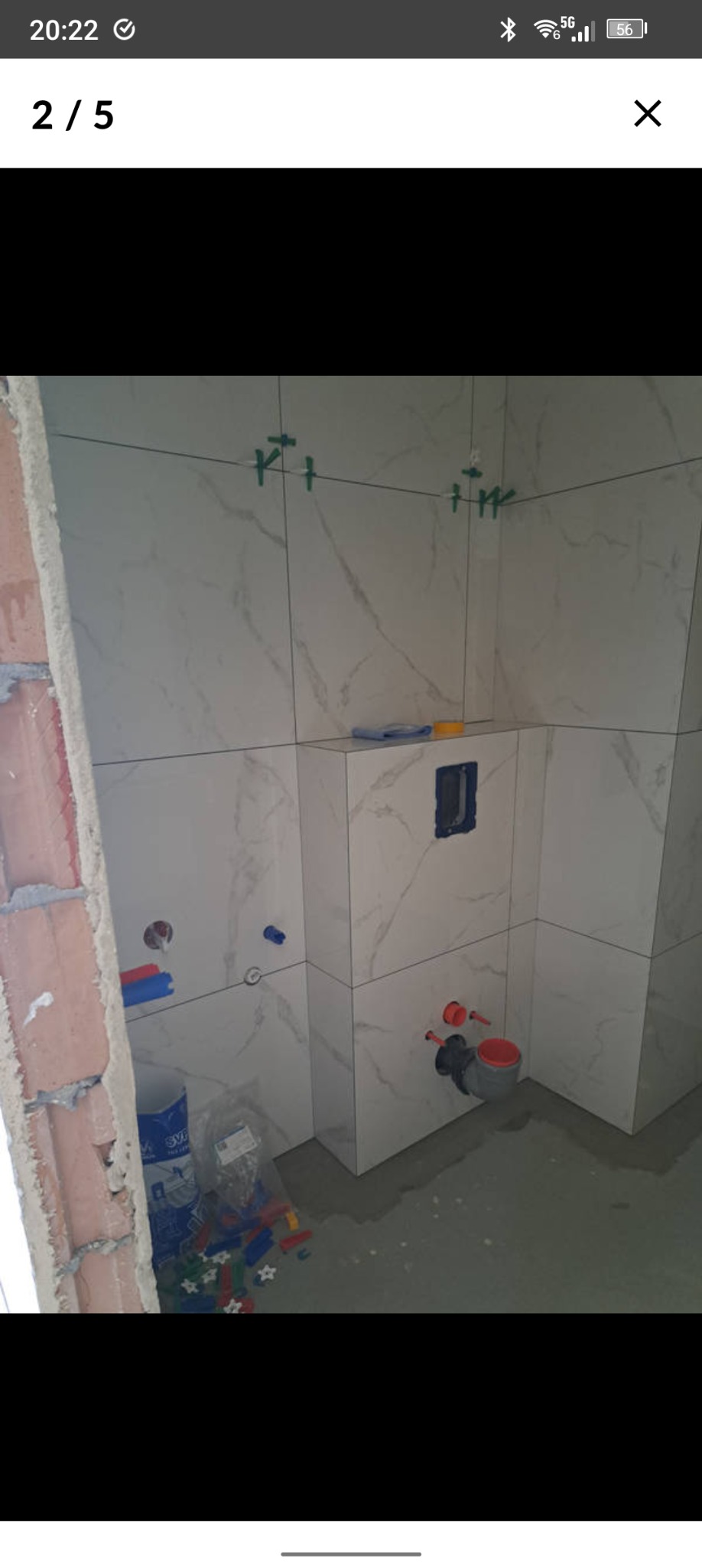 Świeżo ułożone, marmurowe płytki w łazience w Krakowie, z widocznymi elementami instalacji wodnej i poziomującymi klipsami. W tle surowa ściana z cegły.