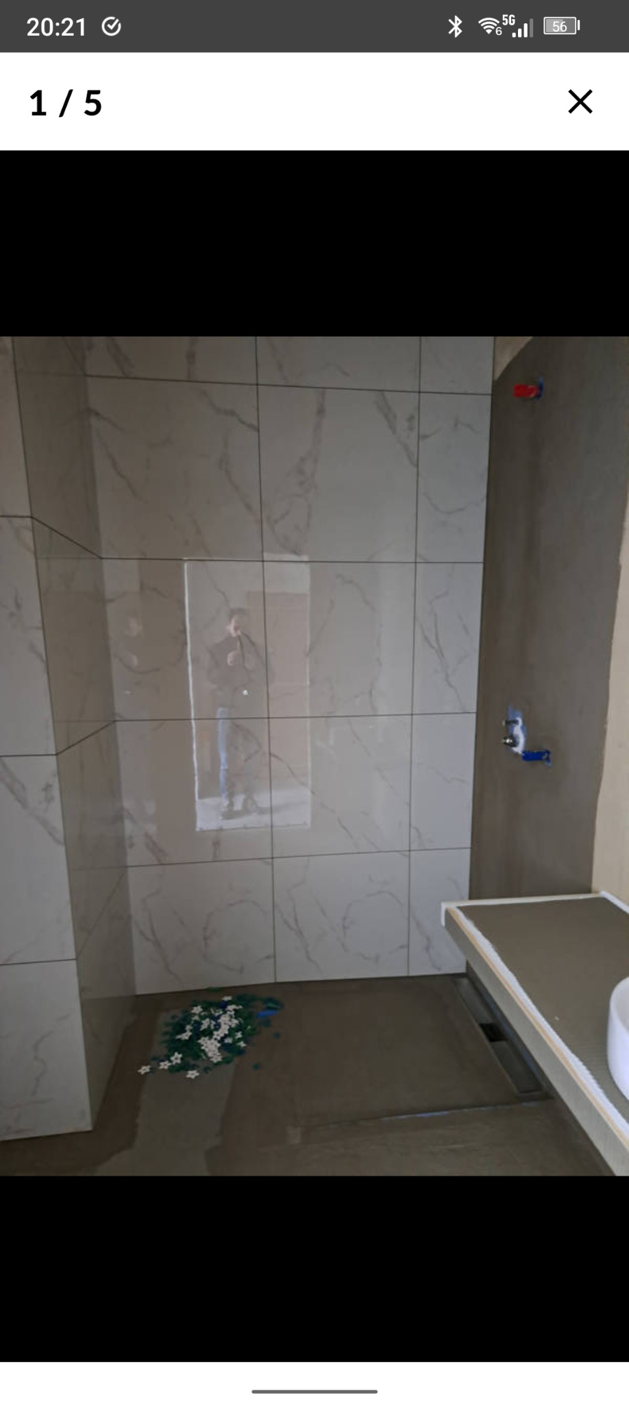 Wnętrze łazienki w trakcie prac. Widoczne płytki imitujące marmur na ścianach, przygotowane miejsce na brodzik i fragmenty płytek na podłodze. Surowy stan wykończenia.