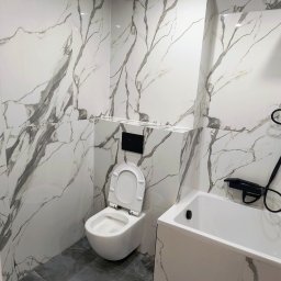 Sergi_job - Wykończona łazienka w bieli i szarości: marmurowe płytki ścienne, szara podłoga, biała wanna i toaleta z czarnym panelem. Nowoczesny design.