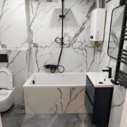 Nowoczesna łazienka z marmurowymi płytkami, czarną armaturą i grzejnikiem. Uwagę przykuwa biały bojler gazowy Ferroli na ścianie.