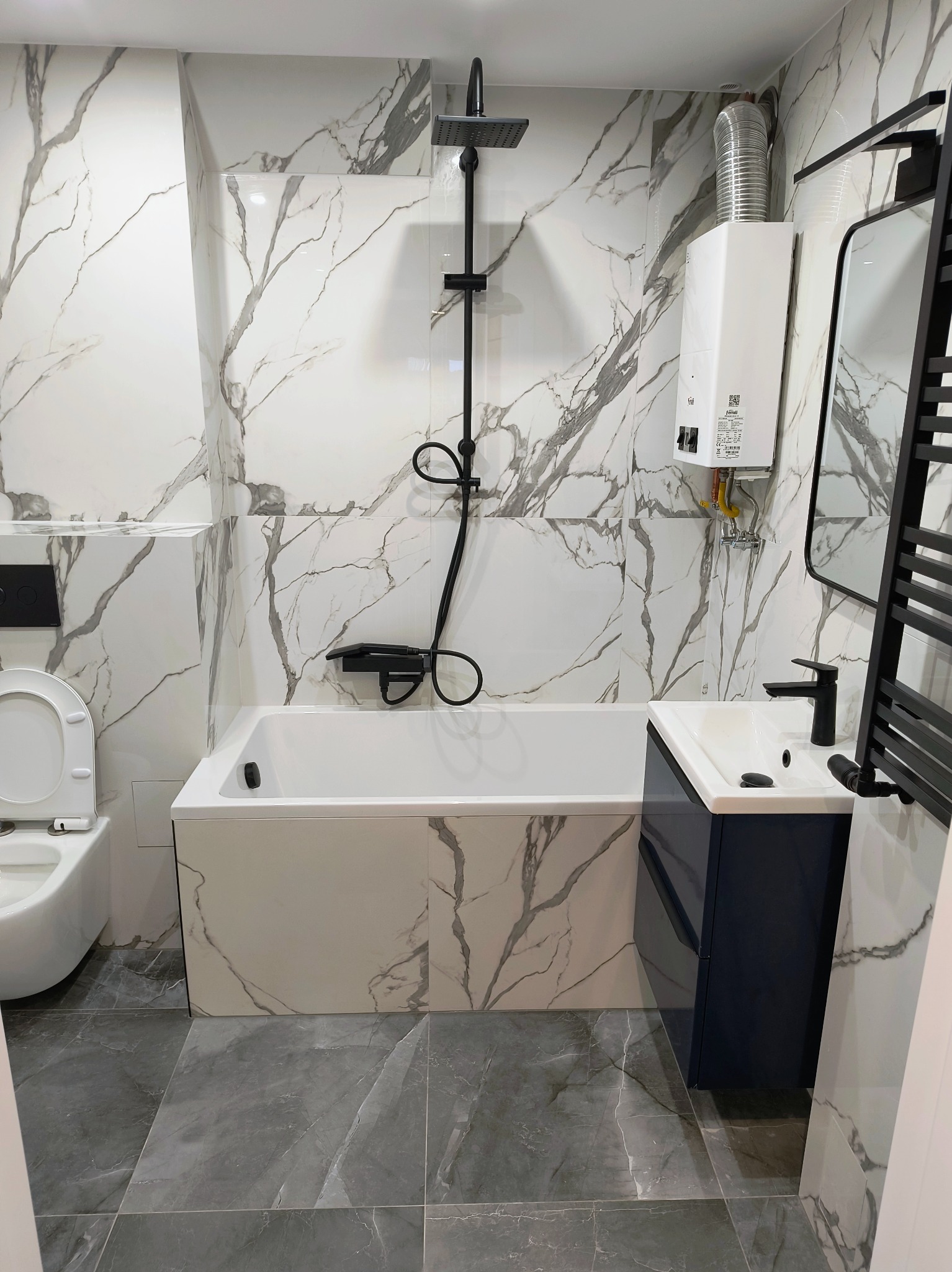 Nowoczesna łazienka z marmurowymi płytkami, czarną armaturą i grzejnikiem. Uwagę przykuwa biały bojler gazowy Ferroli na ścianie.