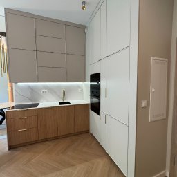 K&K - Nowoczesna kuchnia z drewnianymi frontami szafek dolnych i białymi górnymi, podświetlany blat z marmurowym wzorem, parkiet w jodełkę, piekarnik w zabudowie.