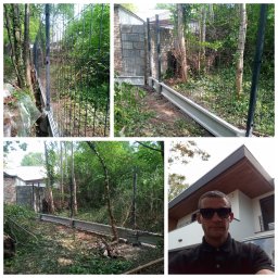 Drzewo PL 76 - Montaż ogrodzenia panelowego z podmurówką betonową na nierównym terenie, obok powalonych gałęzi. W tle budynek z nowoczesną architekturą.