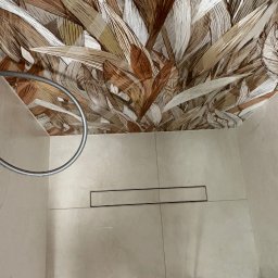 VASYL PAVLIUK Royal Remont - Beżowa łazienka z wzorzystym sufitem w odcieniach brązu i beżu. Widoczny odpływ liniowy, uchwyt na ręcznik i fragment szklanej kabiny. Nietypowe wykończenie sufitu.