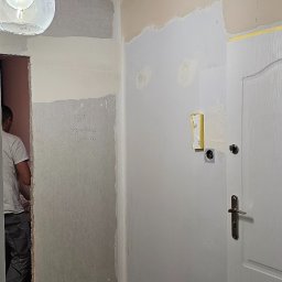 Pawel Wozniak usługi budowlano wykonczeniowe - Wnętrze w trakcie prac wykończeniowych: ściany po szpachlowaniu, widoczna płyta karton-gips, przygotowanie do malowania. Drabina malarska i lampa wisząca w kadrze.