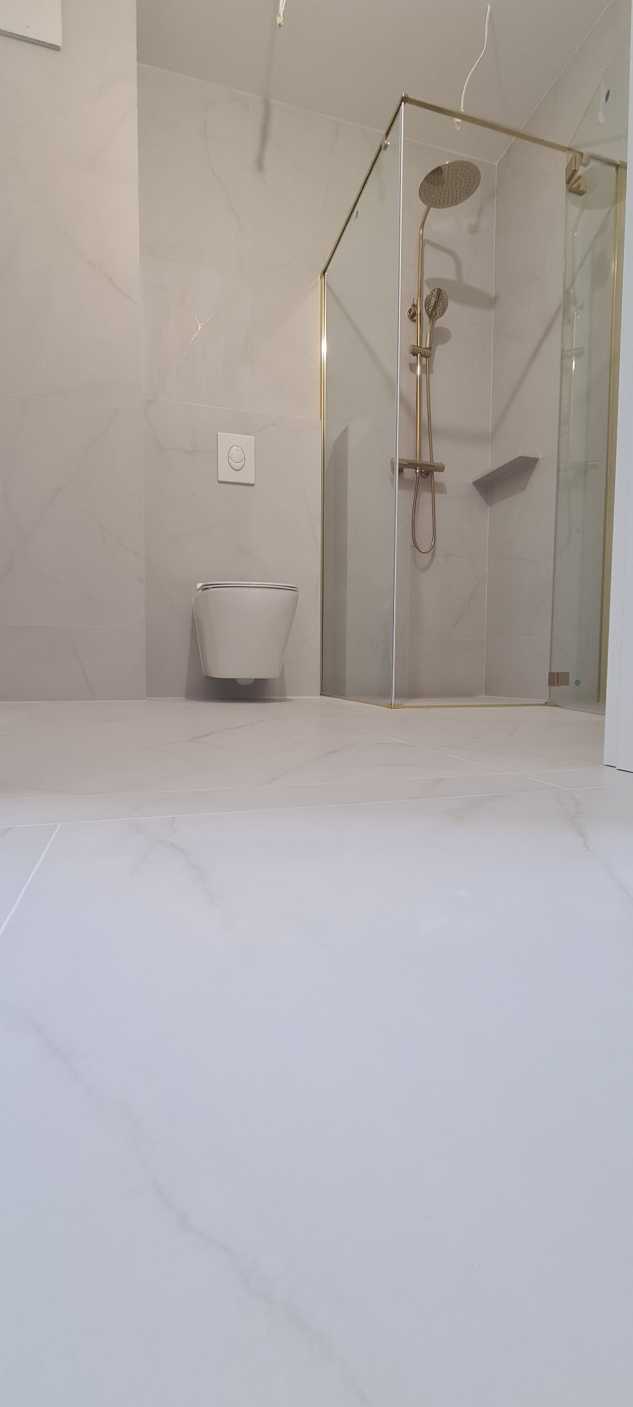 Nowoczesna łazienka z kabiną prysznicową w złotych ramach i podwieszaną toaletą. Minimalistyczny design, jasne płytki imitujące marmur. Wykończenie wnętrz.