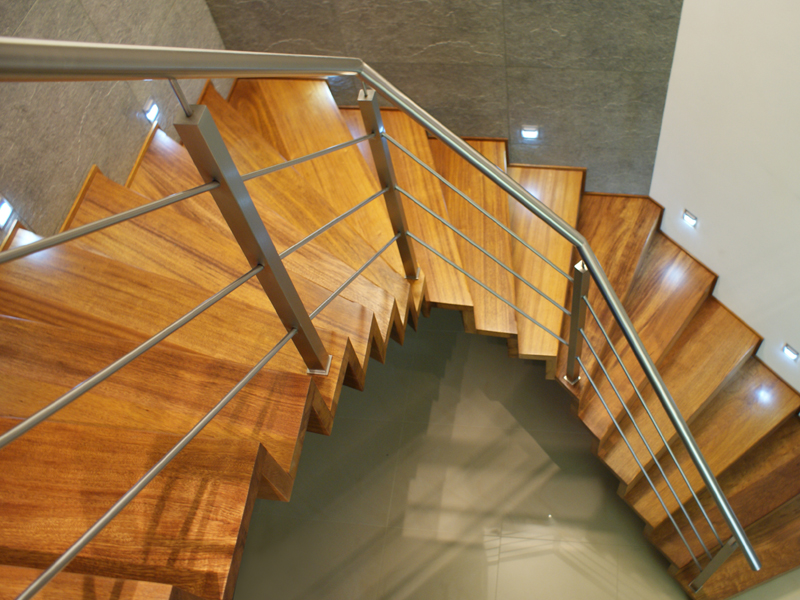 Widok z góry na kręte, drewniane schody z metalową poręczą i podświetleniem LED w stopniach.