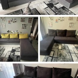 JONATAN KOŁODZIAN - Ciemnoszary narożnik z żółtymi poduszkami na wzorzystym dywanie, widoczny z różnych perspektyw. Na pierwszym planie szary pies. Na ścianie dekoracje.