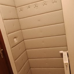 JONATAN KOŁODZIAN - Ukończona realizacja: beżowe panele tapicerowane na ścianie w przedpokoju, z wieszakami i dekoracyjnymi guzikami, tworzące miękkie wykończenie wnętrza.